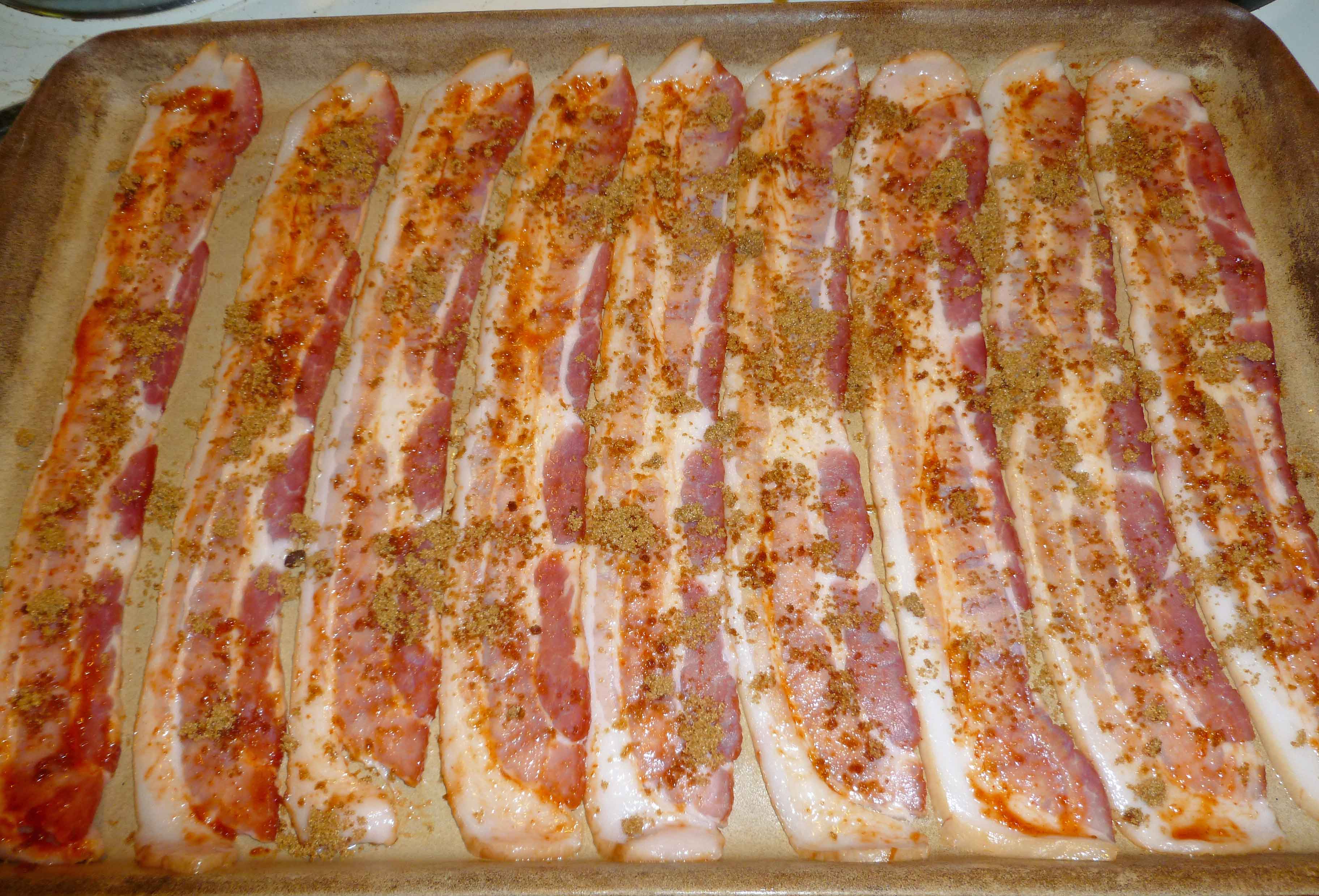 Brown sugar sprinkled over Sriracha covered bacon