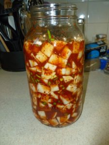 Turnip combined with Korean red pepper flake mixture in jar, pressed down so there are no air pockets