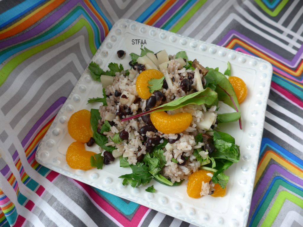 White square plate with dots on the edges, with a green salad topped with a rice mixture and bright mandarin oranges