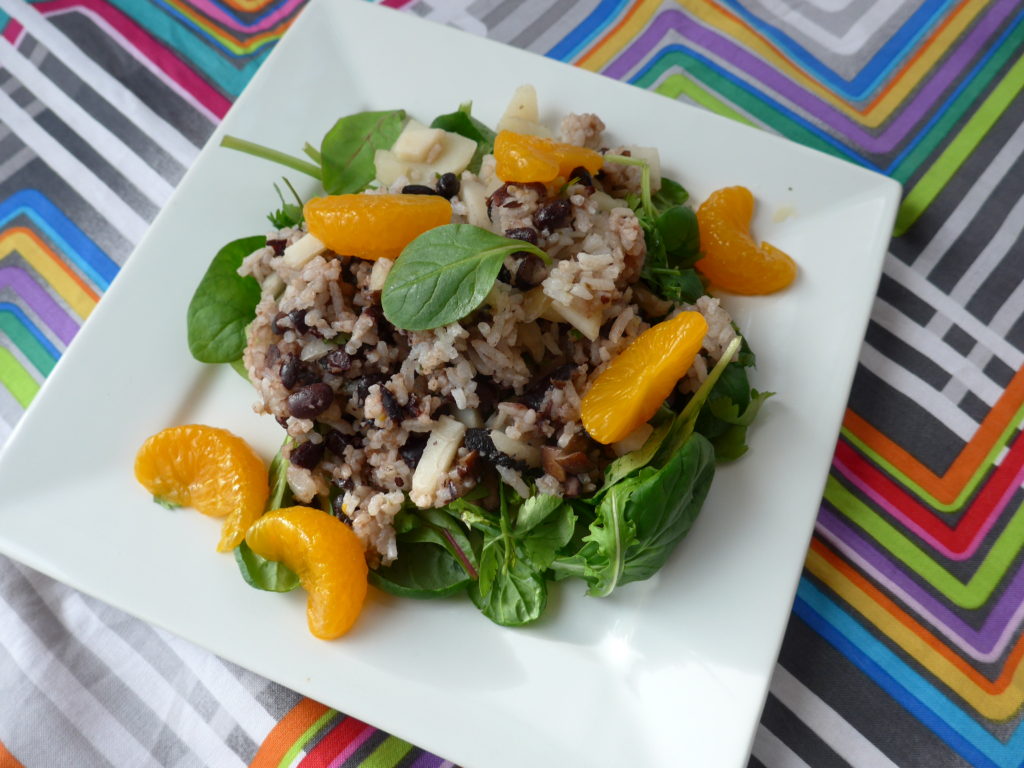 White square plate with dots on the edges, with a green salad topped with a rice mixture and bright mandarin oranges