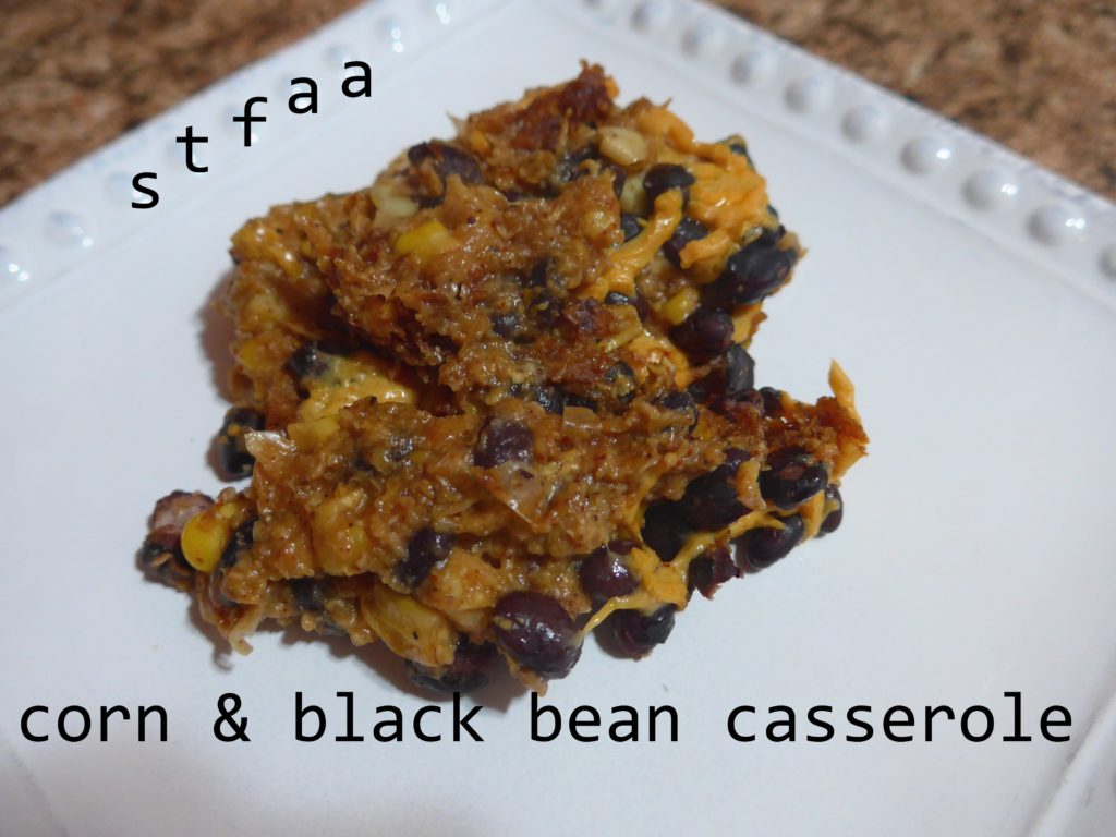 A white plate holds a browned casserole serving with black beans, corn, and cheese