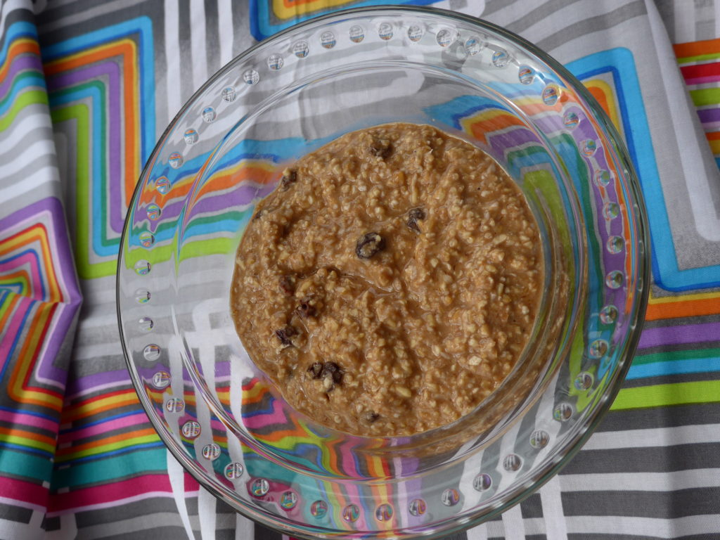 In a clear bowl, light brown porridge with raisin, on a brightly colored backdrop