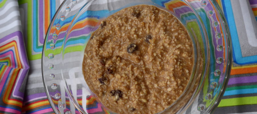 In a clear bowl, light brown porridge with raisin, on a brightly colored backdrop