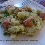 Image shows a pile of green cabbage and salmon cubes with a potato dill and scallion "sauce" on a white plate with a fork in the background